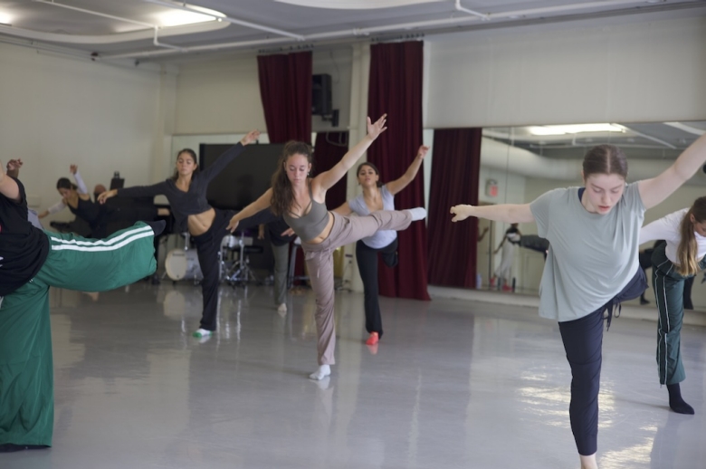 Dancers stand on one leg with arms extended during class in a dance studio